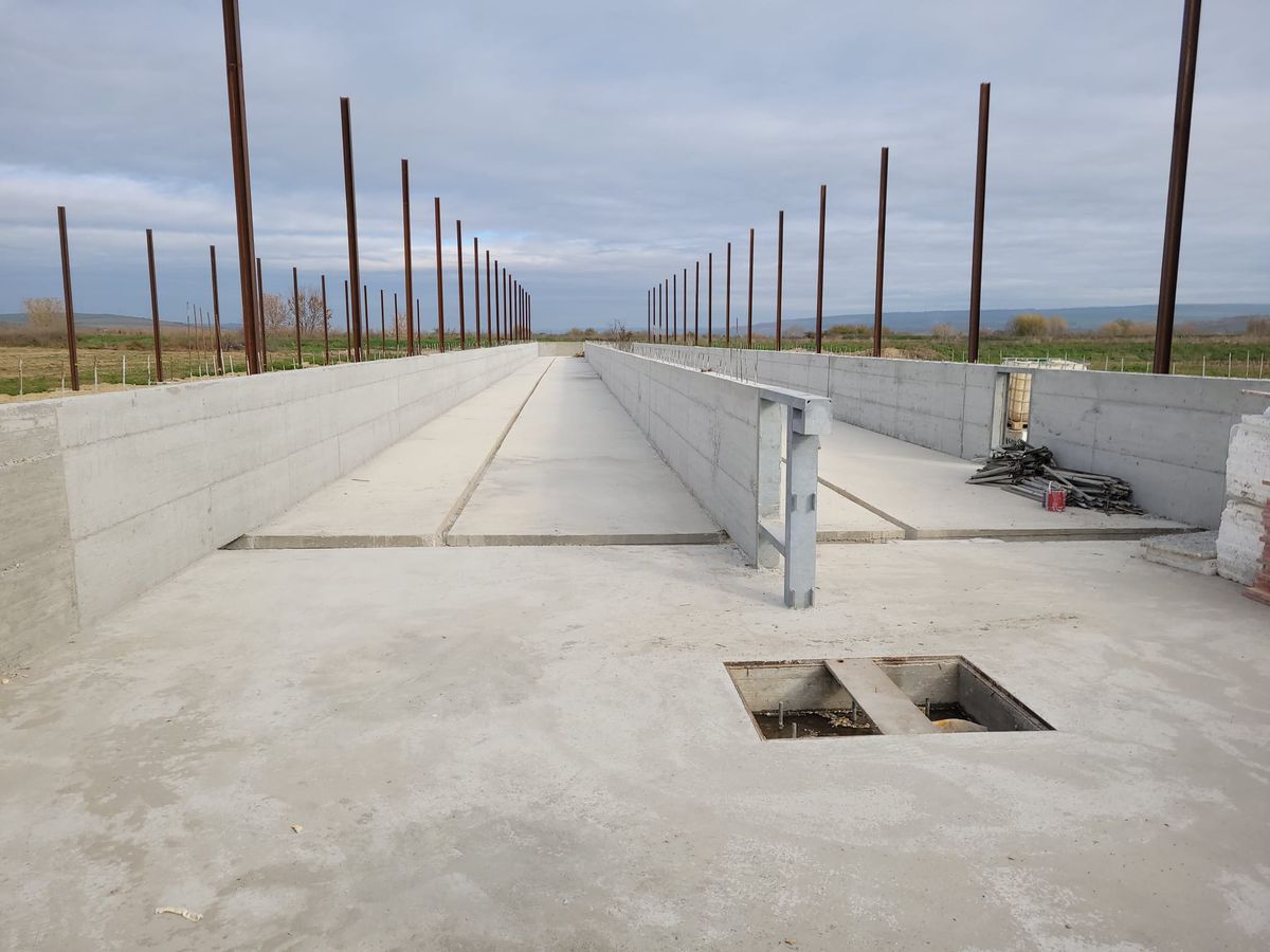 Culoar de beton cu pereți laterali și rând de stâlpi metalici, pe un șantier de hală