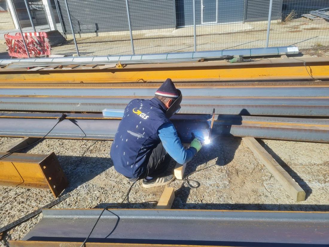 Sudor care îmbină grinzi de oțel pentru o hală metalică, pe șantier