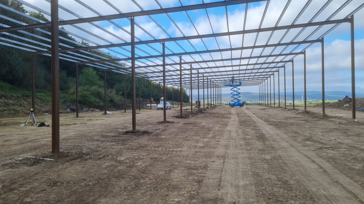 Structură metalică lungă de hală cu ferme de acoperiș, pe un teren în pantă